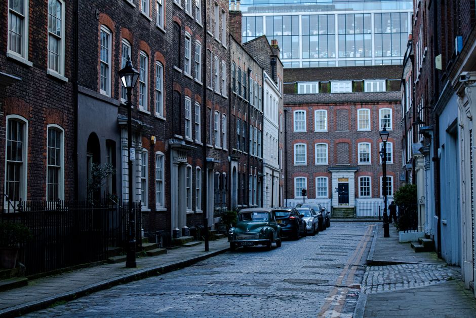 A street scene in Fitzrovia with a clear blue sky overhead. On the right side, there is a building with large windows and colorful flags hanging from the facade, which belong to a retail store or comm