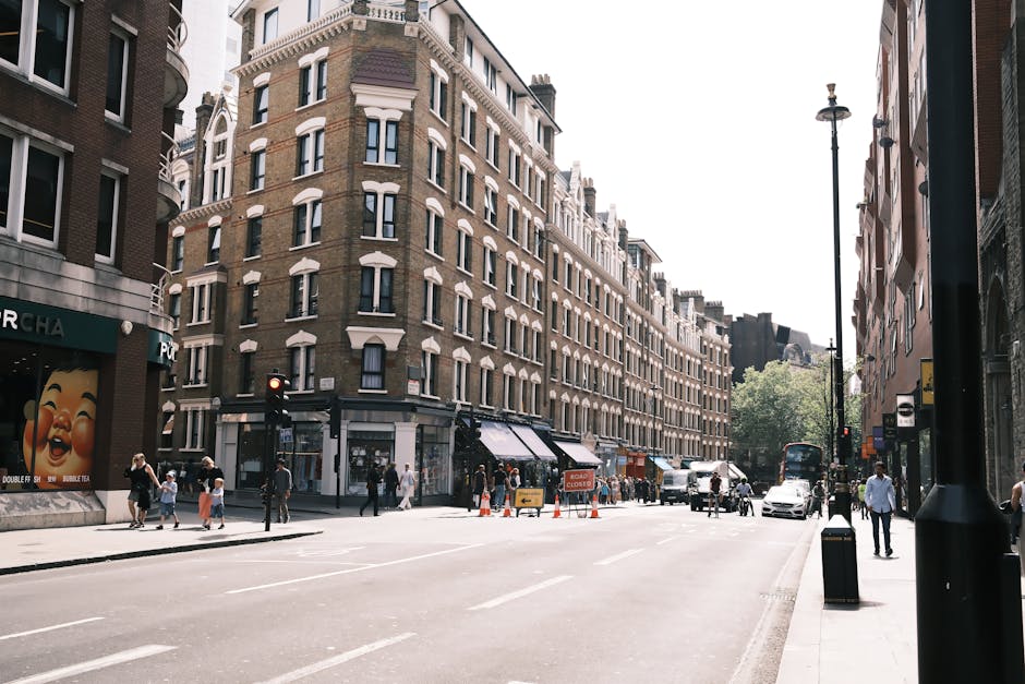 View of a street scene in Fitzrovia showing the exterior of a building with large bay windows, decorative architectural details, and a wooden ground-floor facade, alongside a lamppost with an orange s