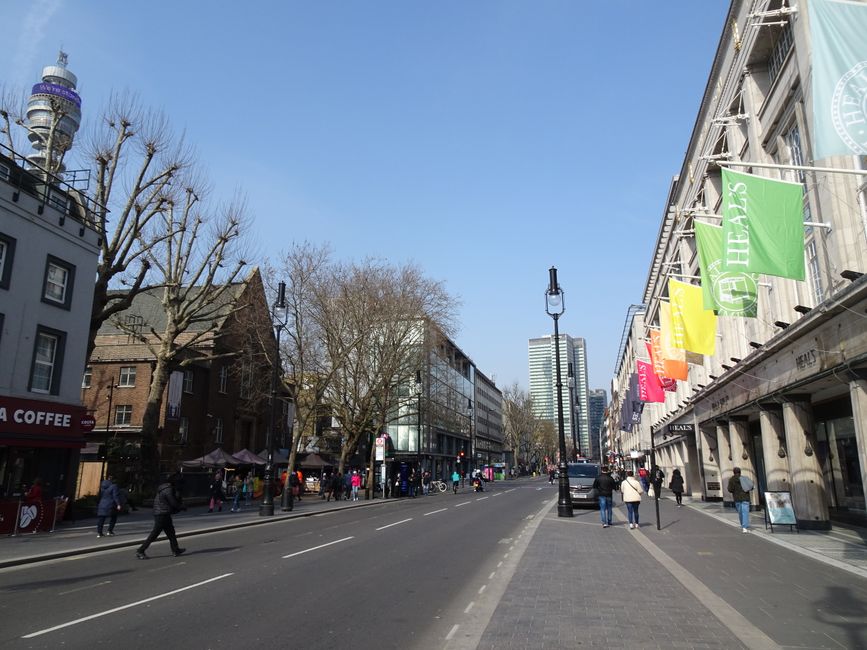 Close-up image of a building corner showing a white and red sign indicating the Bell Yard WC2 parking suspensions for Westminster, UK, with text 'CITY OF WESTMINSTER'. Below the sign, a yellow notice warns that 24-hour CCTV is in operation and fly-tippers will be prosecuted. To the left, a dome-shaped CCTV camera is mounted on the wall, aimed at the street to monitor parking and loading activities. On the right side, part of a decorative street lamp with a white spherical light is visible, attached to a black metal post. The background features a clear blue sky with a tree branch partially visible at the top. The setting suggests the signage is part of the infrastructure supporting house and furniture removals, ensuring designated parking and security during home relocation or moving services carried out by [COMPANY_NAME].